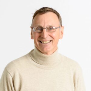 Foto von Dr. Hans-Joachim Büttner. Er lächelt freundlich und hat kurze braun-graue Haare. Er trägt eine Brille und einen beigen Rollkragenpulli.