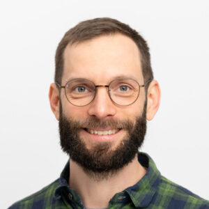Foto von Jari Trabert. Er lächelt freundlich, hat braune kurze Haare und einen Bart. Er trägt eine Brille.