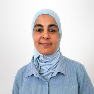 Foto von Karema El Messaoudi. Sie lächelt freundlich. Sie trägt eine hellblaue Bluse und ein hellblaues Kopftuch. Sie hat braune Haut.