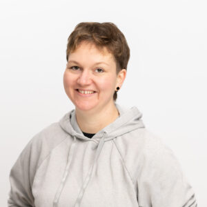 Foto von Katharina Reisinger. Sie lächelt freundlich und hat helle Haut und dunkelblonde kurze Haare. Sie trägt einen hellgrauen Kapuzenpulli.