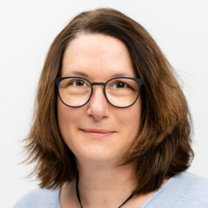 Foto von Marion Lamberz. Sie lächelt freundlich, hat braune schulterlange Haare und helle Haut und trägt eine Brille.