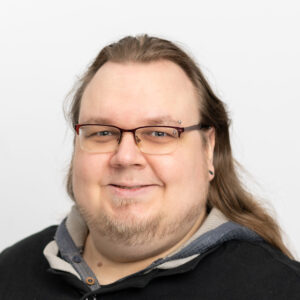 Foto von Matthias Hodurek. Er lächelt und hat lange dunkelblonde Haare und eine Brille.