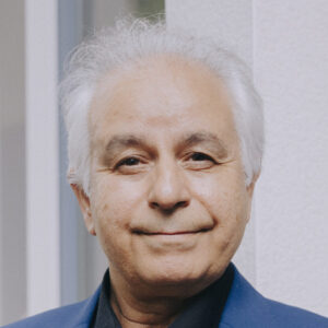 Foto von Dr. Dr. Rahim Schmidt. Er lächelt, hat weiße Haare und hellbraune Haut.