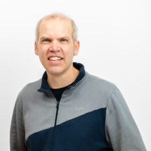 Foto von Dr. Sebastian Schink. Er lächelt freundlich. Er hat helle Haut und wenige kurze grau-blonde Haare. Er trägt einen grau-blauen Pulli.