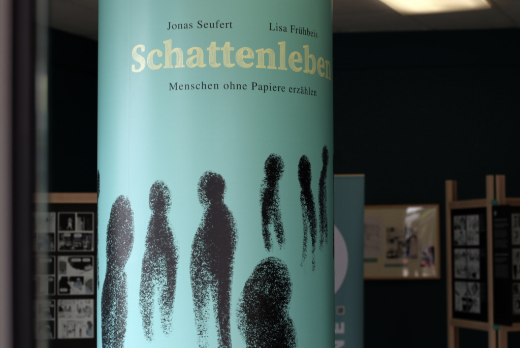 Ein Foto von der Ausstellung. Man sieht groß den Buchtitel und dahinter klein verschiedene Ausstellungstafeln.